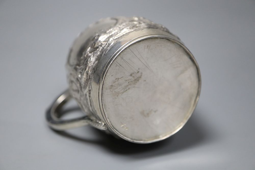 A George III silver barrel shaped christening mug, embossed with figures at play in woodland scene,